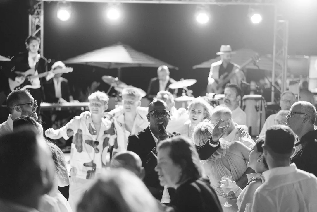 Inan Lima singt mitten auf der Tanzfläche zwischen feiernden Hochzeitsgästen, im Hintergrund die Live-Band mit Gitarre, Drums und Percussion auf der Bühne – Hochzeitsband Mallorca